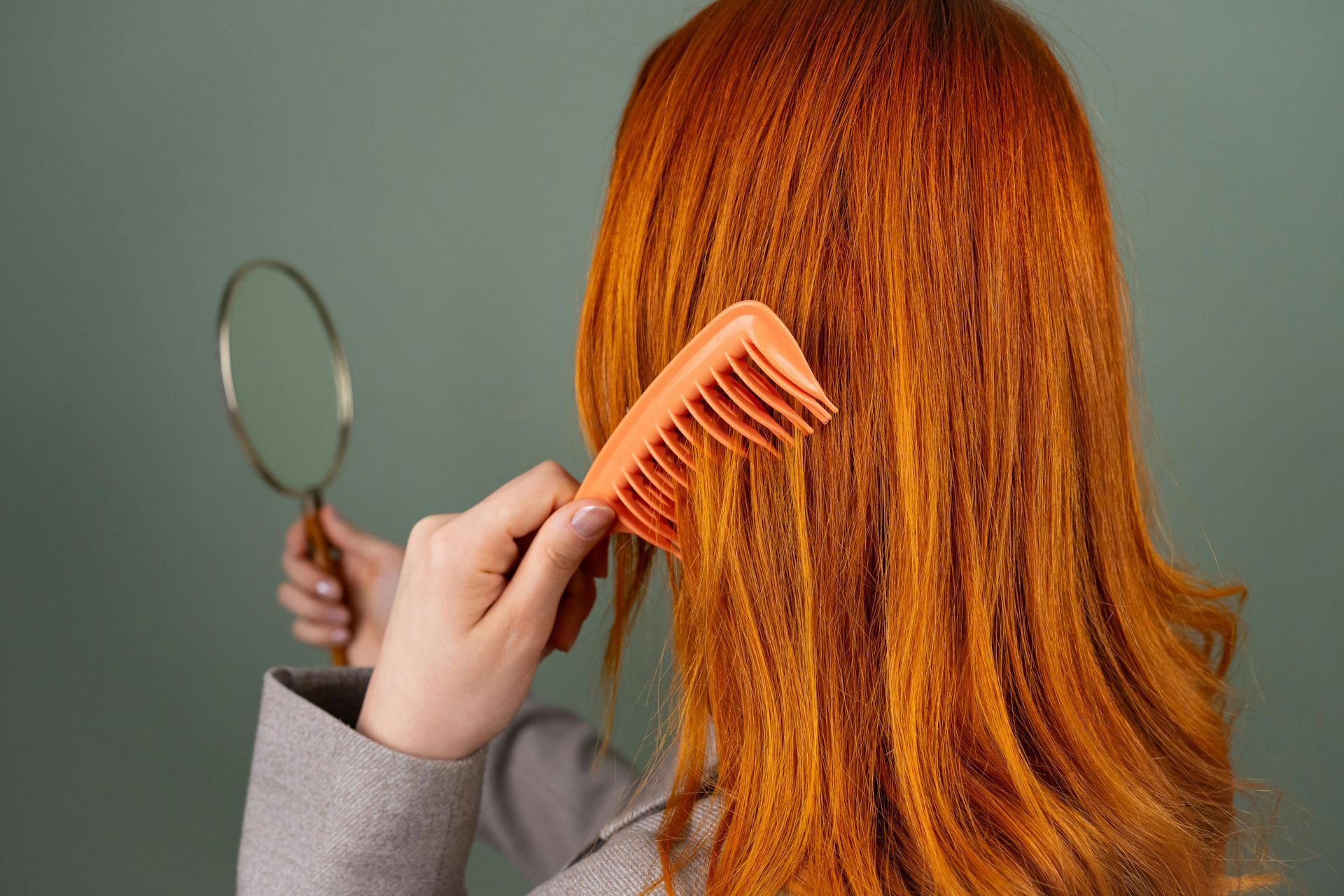 A woman is combing her red hair in front of a mirror.