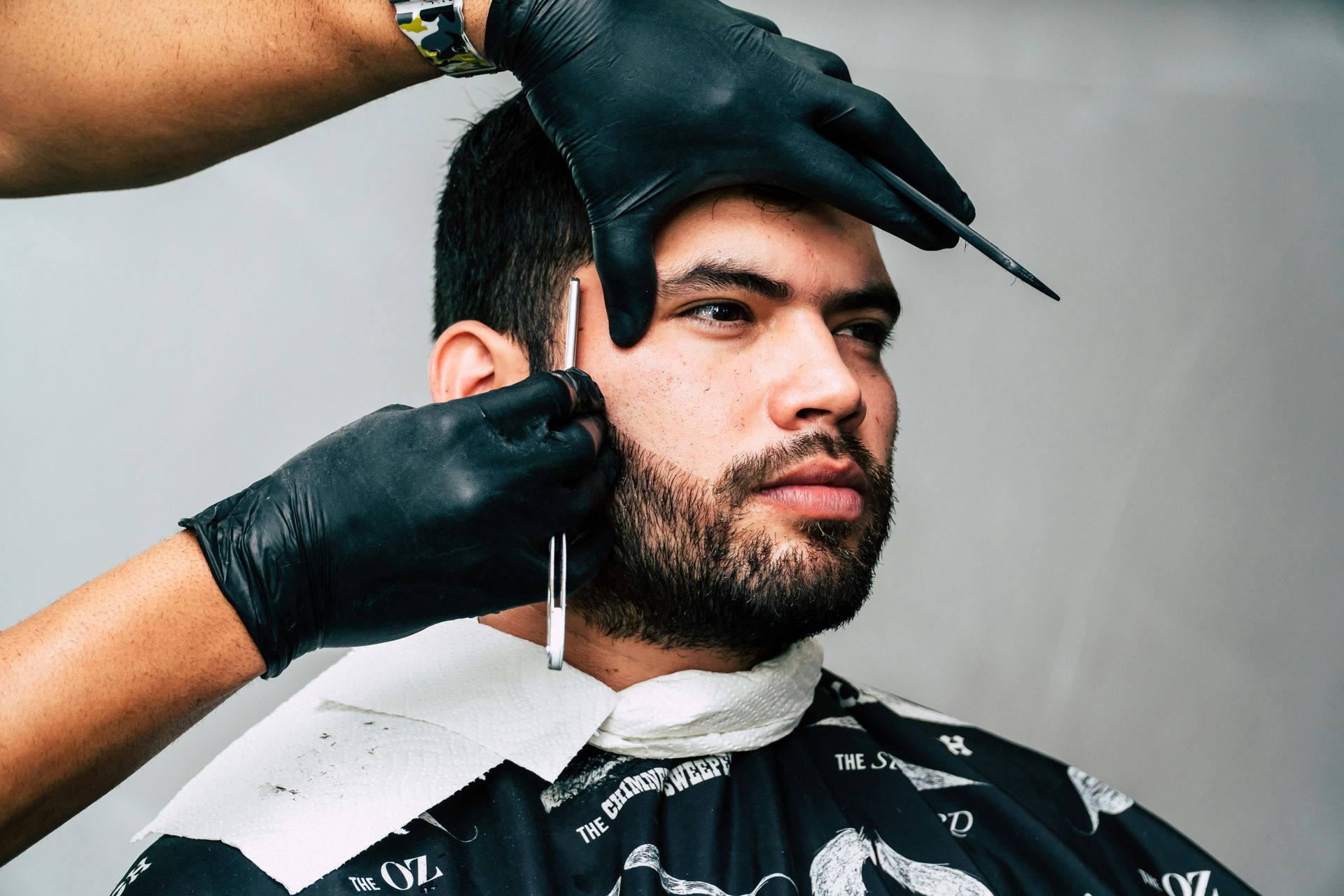 A man is getting his beard shaved by a barber wearing black gloves.