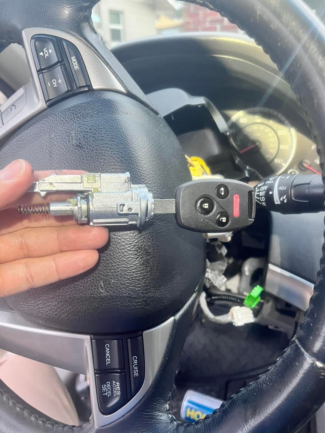 Hand holding a car ignition cylinder and key near a steering wheel, showing removal.
