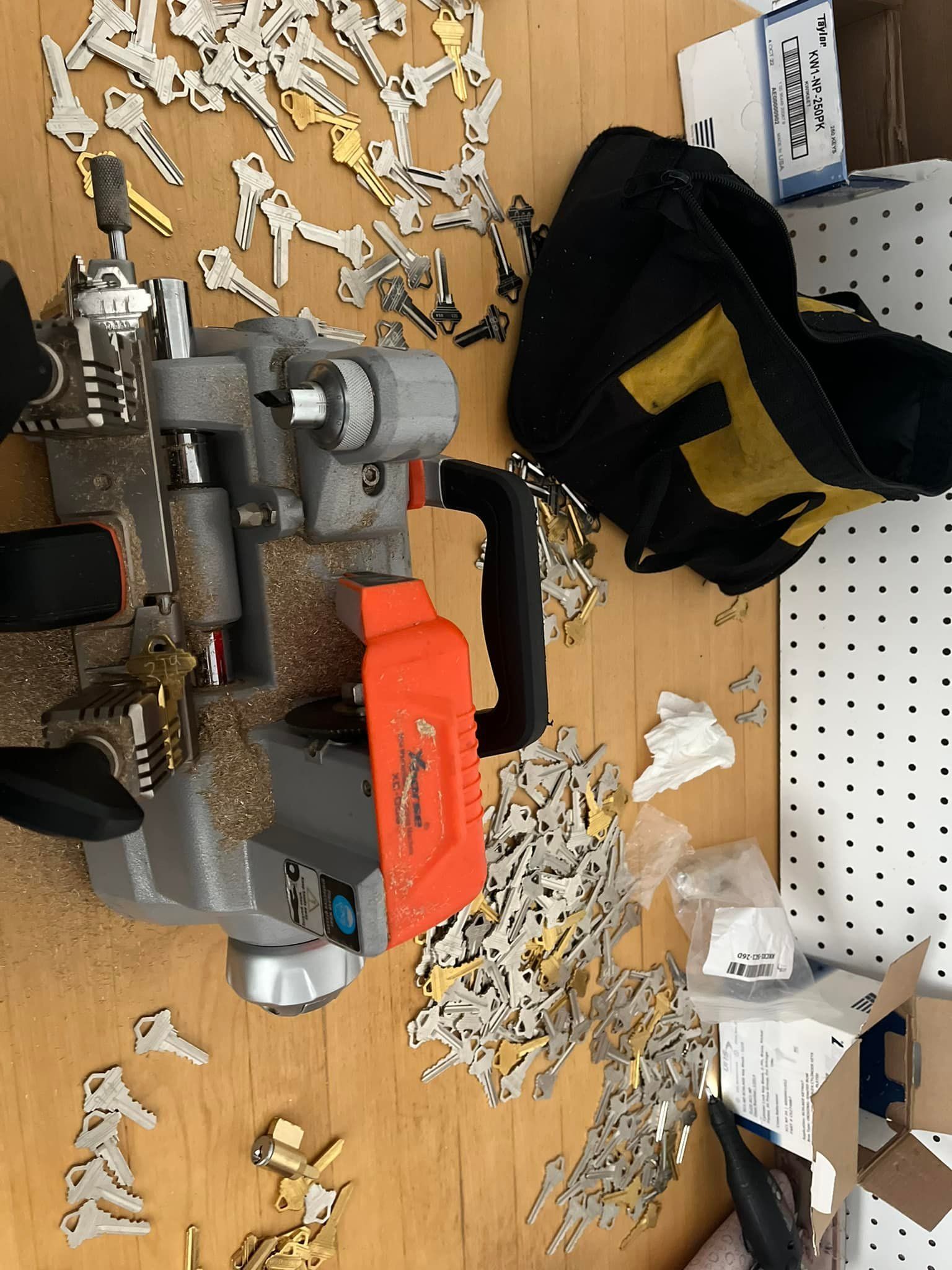 Key cutting machine with a pile of keys, a black bag, and scattered key blanks on a wooden surface.