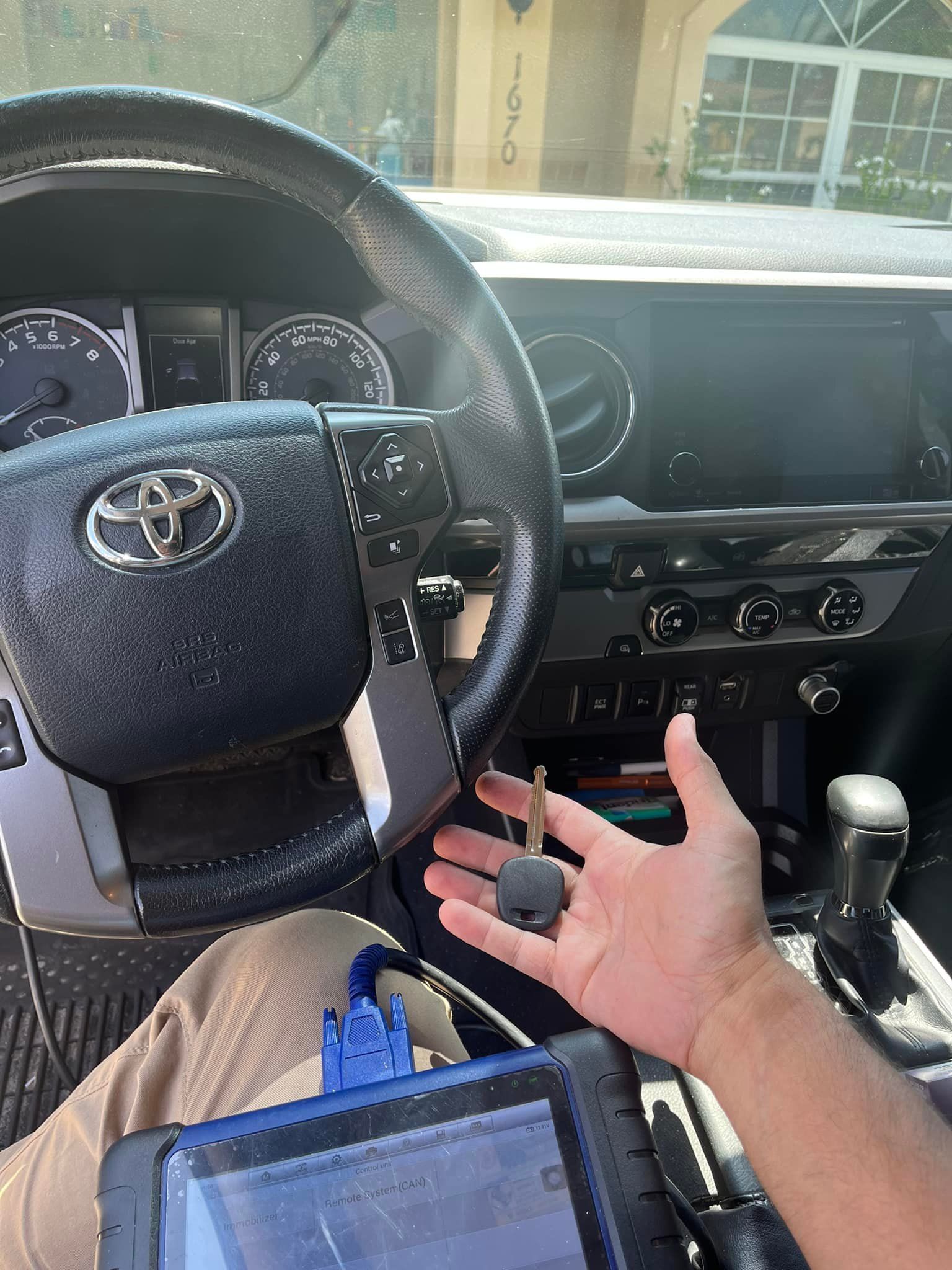 Person holding car key inside a Toyota. Dashboard and diagnostic tool are visible.