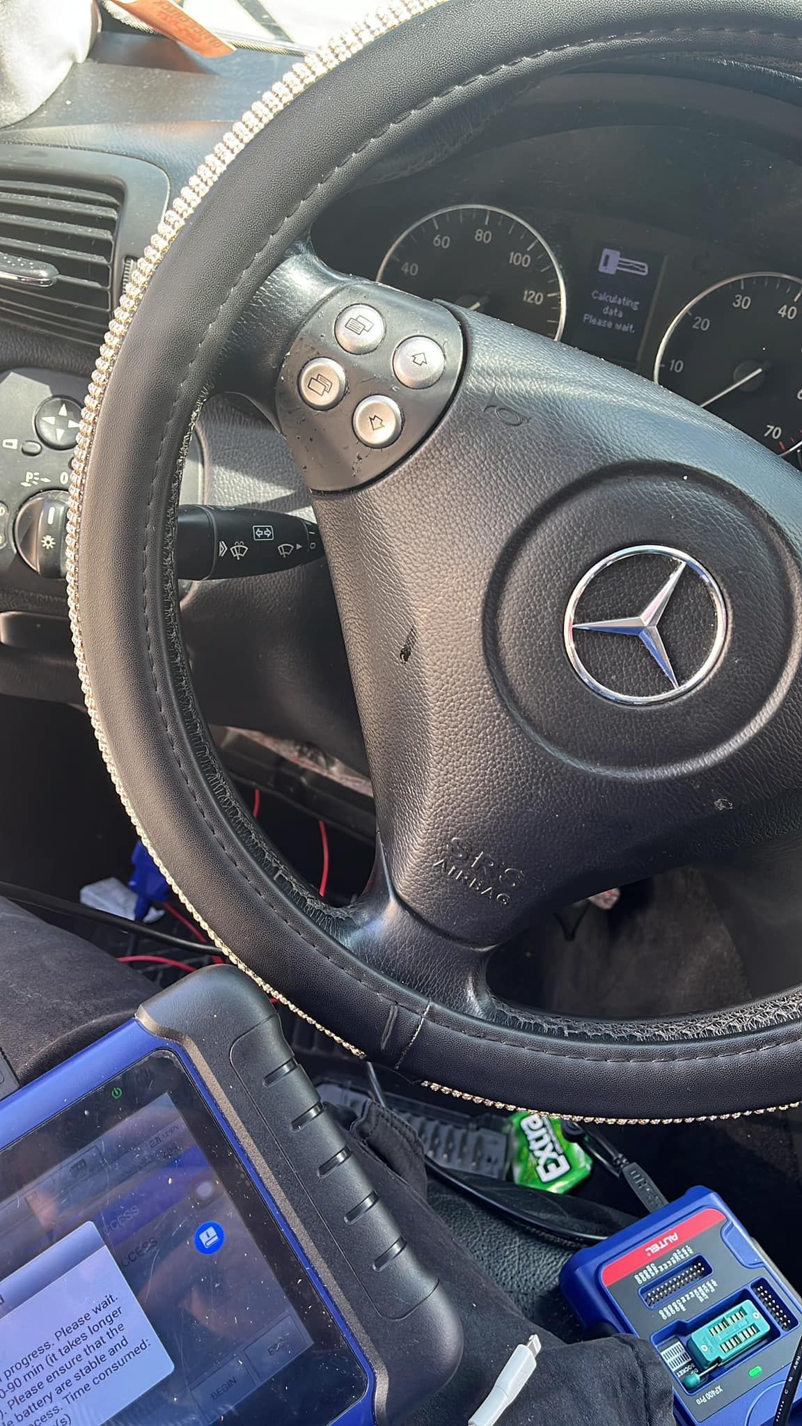 Black Mercedes steering wheel with dashboard, diagnostic tools, and a rhinestone-covered rim.