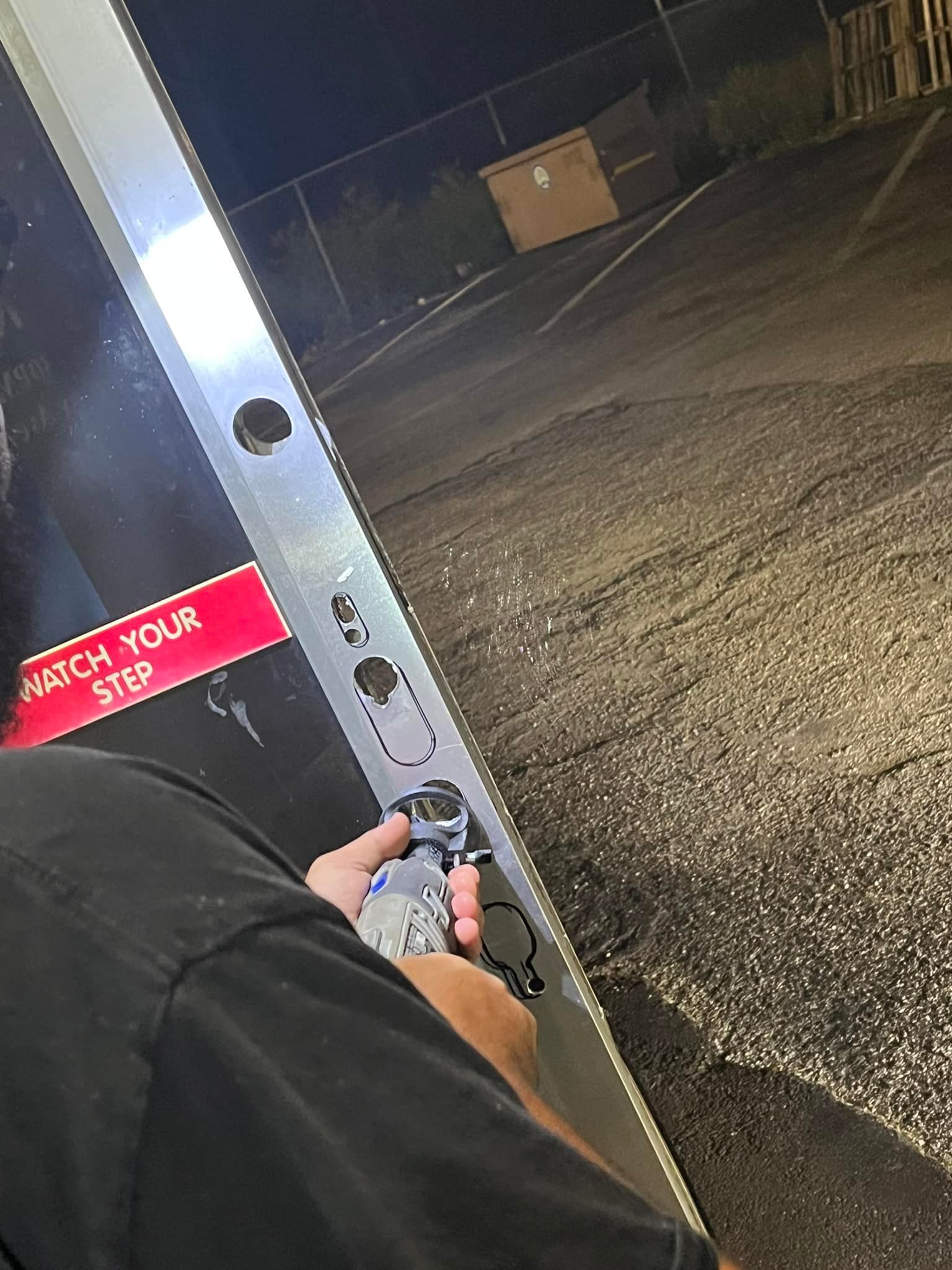 Person drilling into a doorframe outside at night; a red