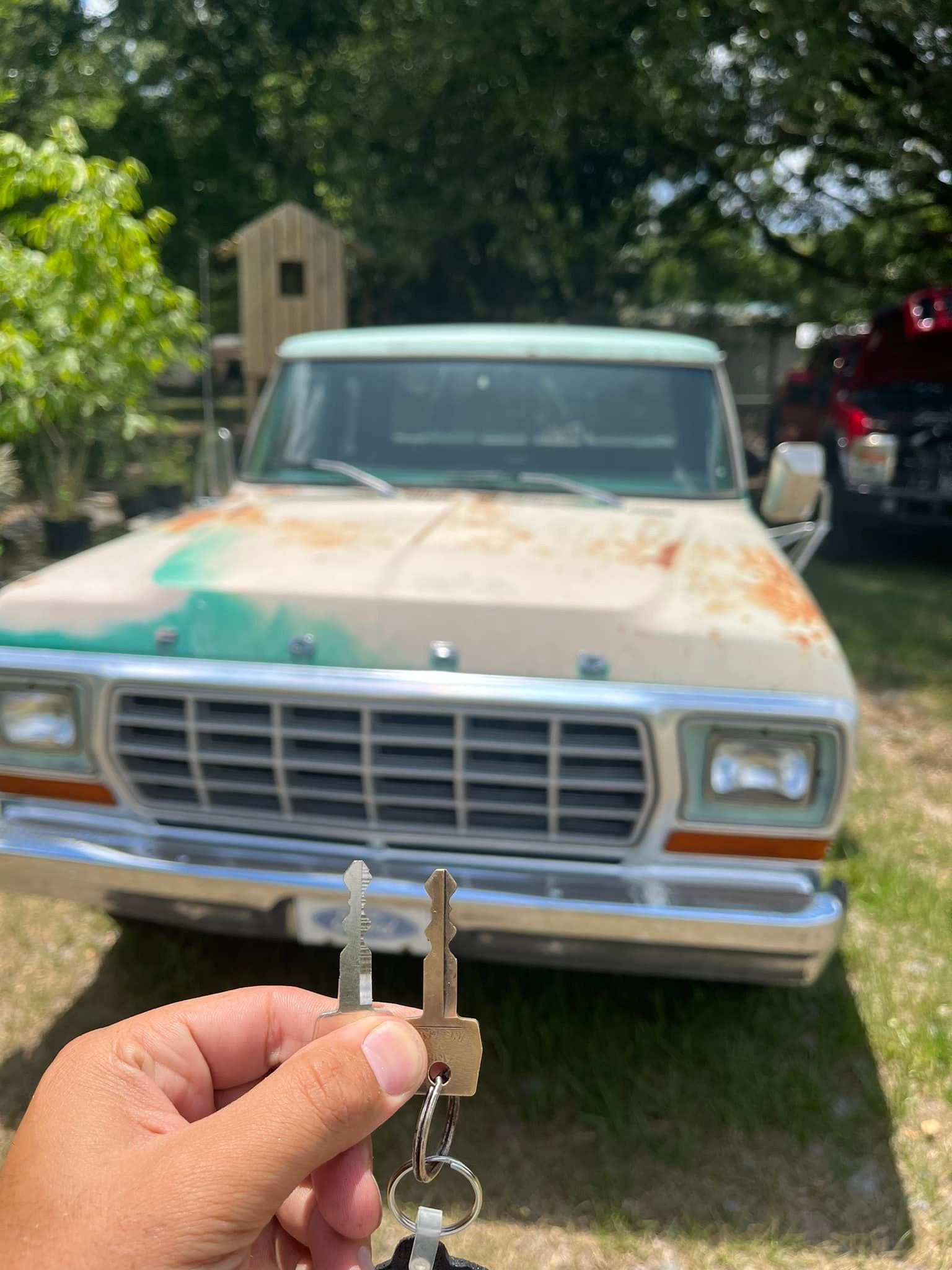 Hand holding keys in front of a weathered beige Ford pickup truck, in an outdoor setting.
