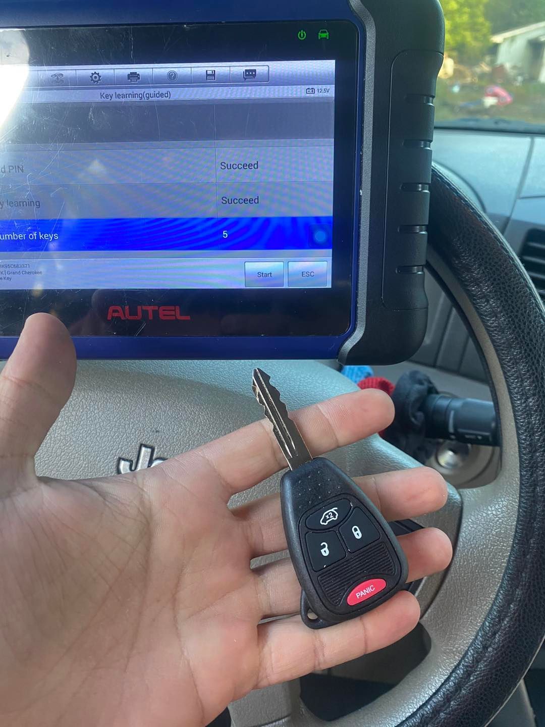 Hand holding a Jeep key with a diagnostic scanner in the background, displaying
