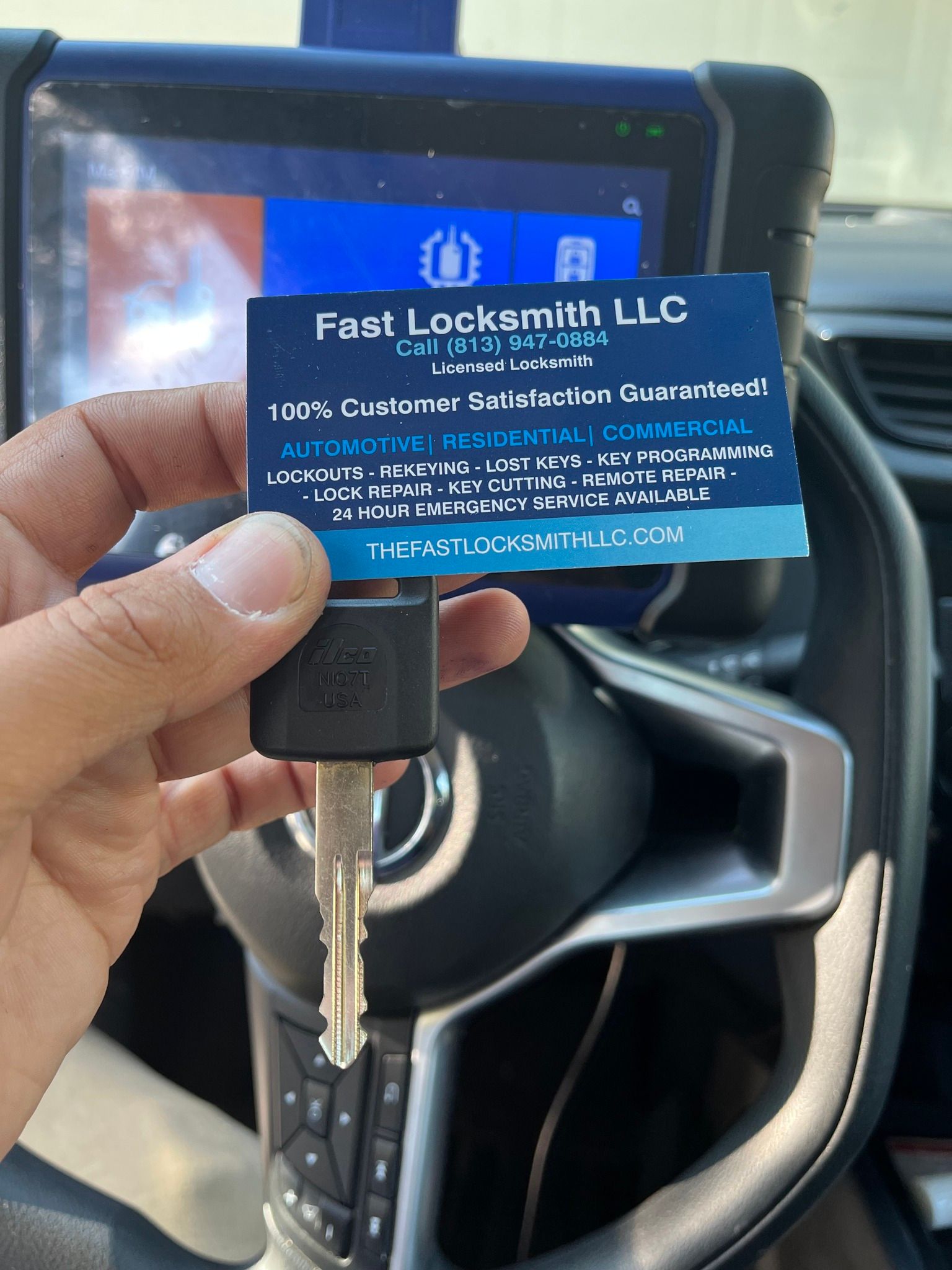 Hand holding a key, business card for Fast Locksmith, car interior.