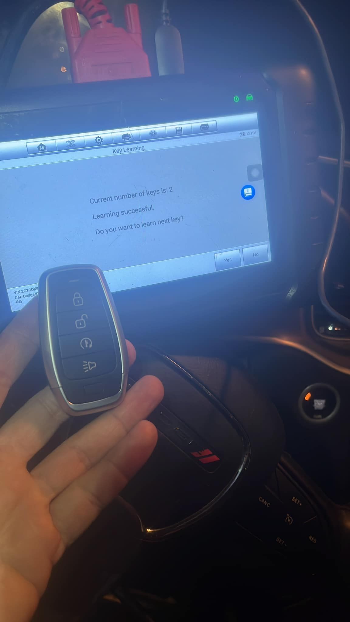 Hand holding a car key in front of a car dashboard screen displaying