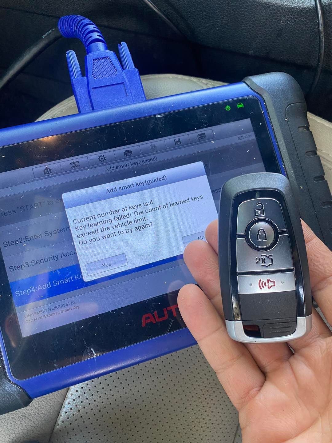 A hand holds a Ford key fob next to a diagnostic tool displaying a failed key programming message.