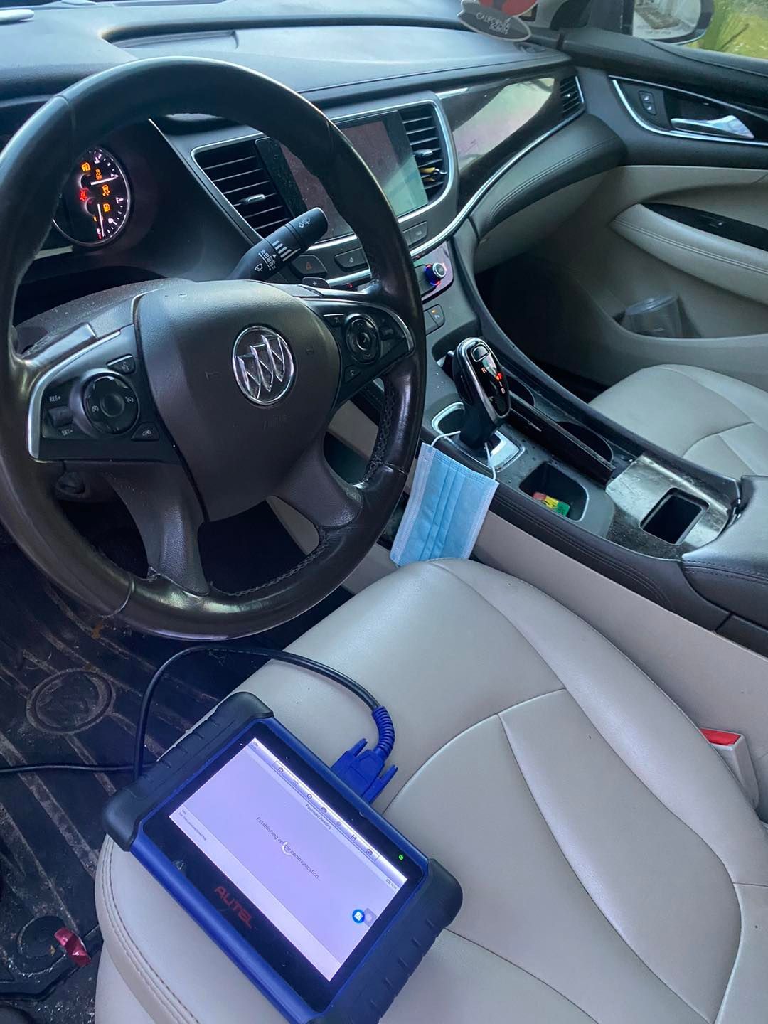A person inside a Buick car is using a diagnostic tool on the front seat, likely for car maintenance.