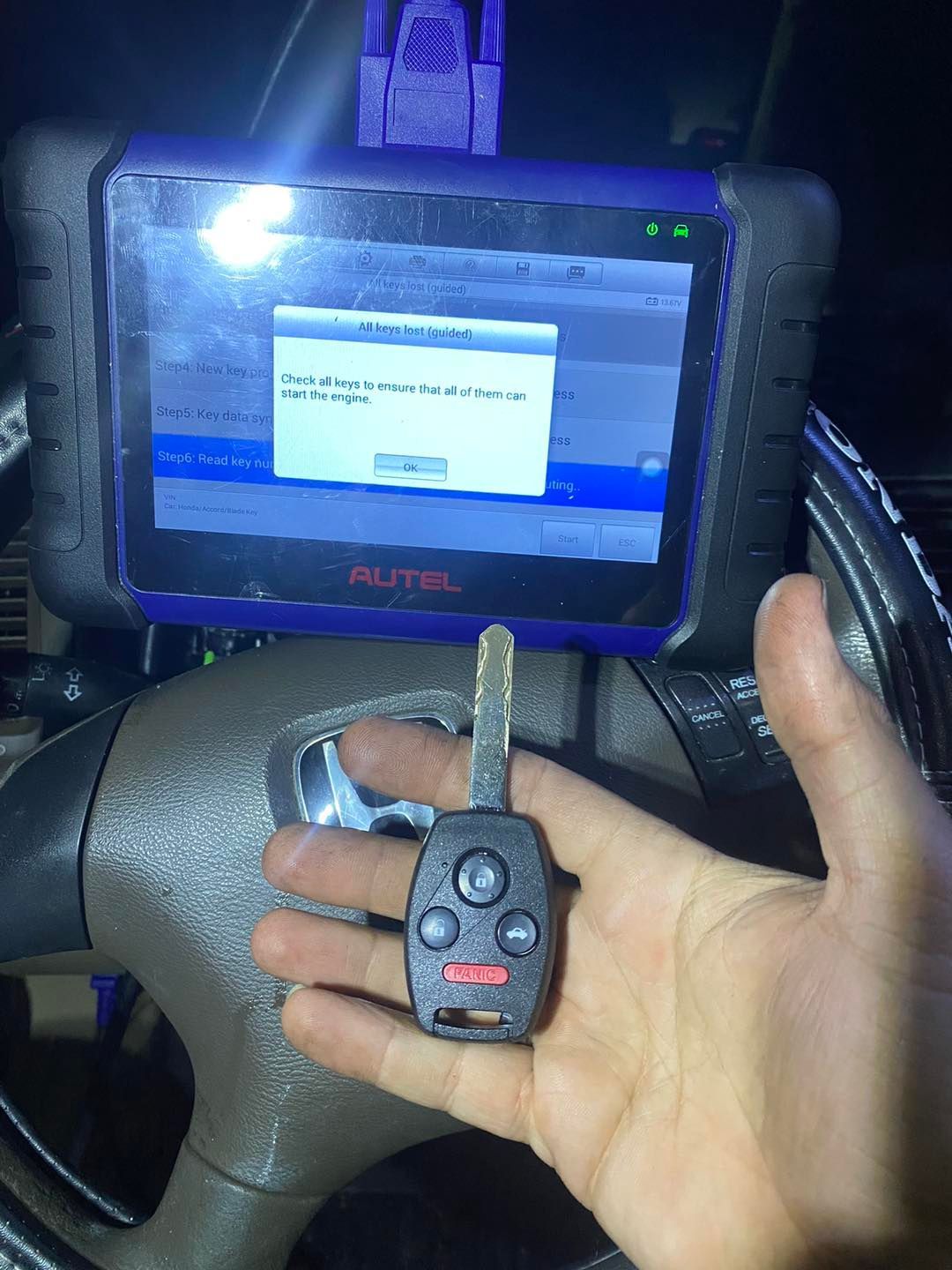 A person holding a car key near a diagnostic tool screen in a car; shows a key-programming message.