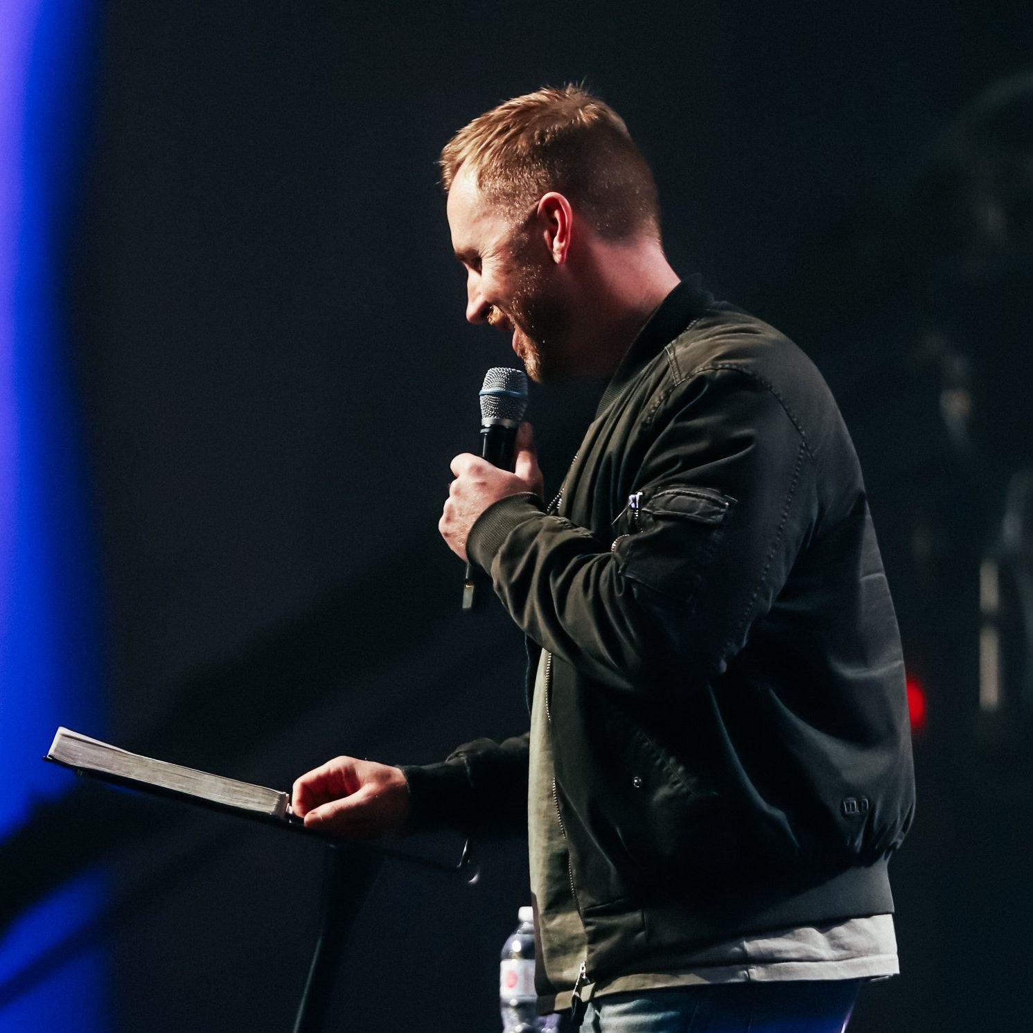 A man speaking into a microphone while holding a book