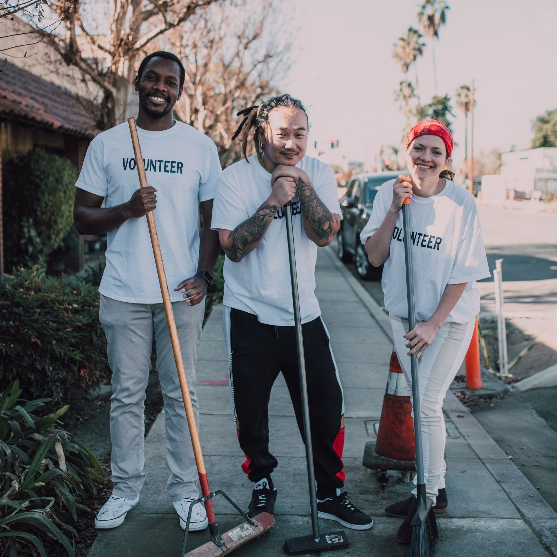 Three people wearing volunteer shirts are standing on a sidewalk
