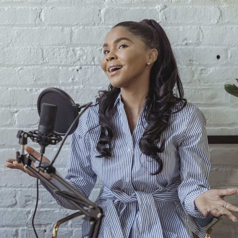A woman is singing into a microphone in front of a white brick wall.