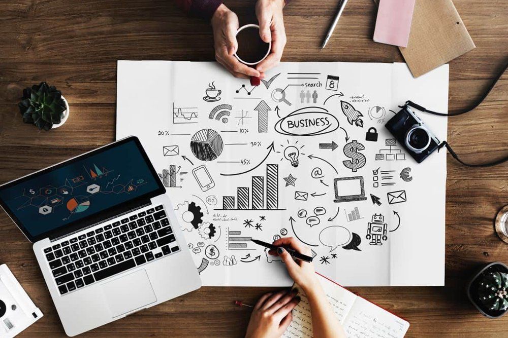 A couple of people are sitting at a table with a laptop and a notebook.
