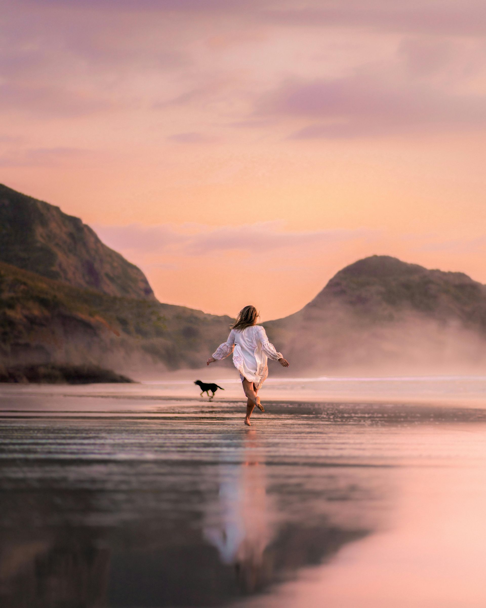 A woman is walking a dog on a beach at sunset.