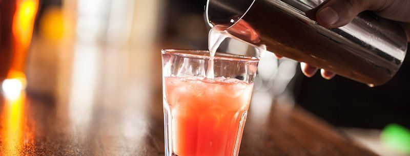 A bartender is pouring a drink from a shaker into a glass.