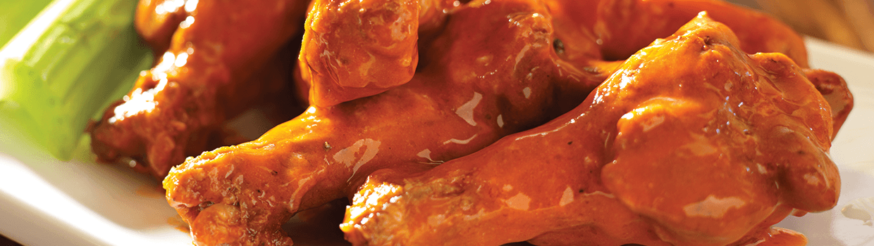 A close up of a plate of chicken wings with celery on a table.