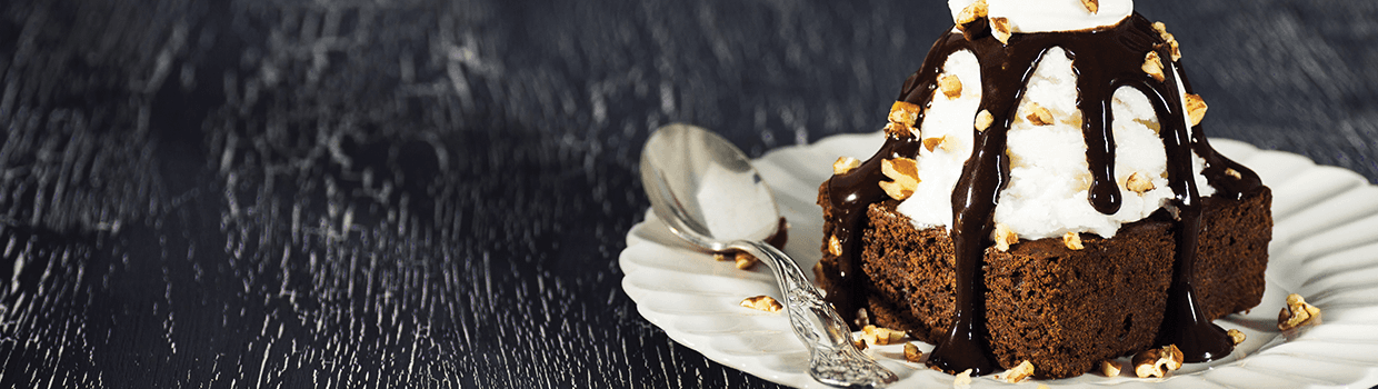 A chocolate cake with marshmallows and chocolate sauce on a paper plate.