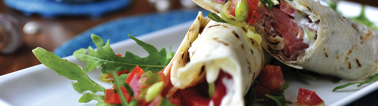 A close up of a tortilla wrap with tomatoes and lettuce on a plate.