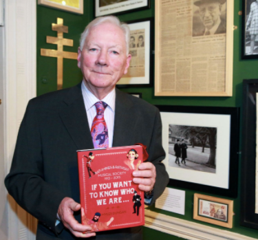 A man in a suit and tie is holding a book titled if you want to know who we are