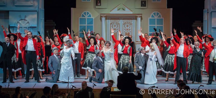 A large group of people are dancing on a stage in front of an orchestra.