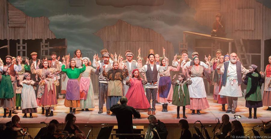 A large group of people are standing on a stage in front of an orchestra.