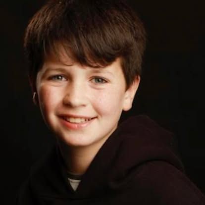 A young boy wearing a black hoodie is smiling for the camera.