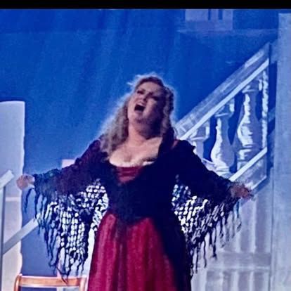 A woman in a red dress is singing on a stage.