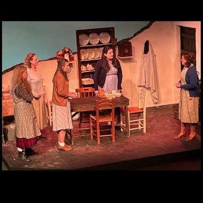 A group of women are standing around a table on a stage.