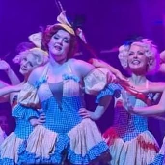 A group of women in blue and white dresses are dancing on a stage.