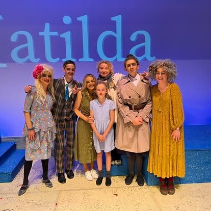 A group of people are posing for a picture in front of a sign that says atilda.