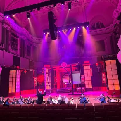 A group of people are playing instruments on a stage with purple lights.