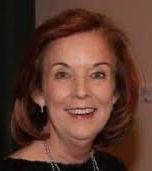 A woman with red hair is smiling and wearing a black shirt and earrings.