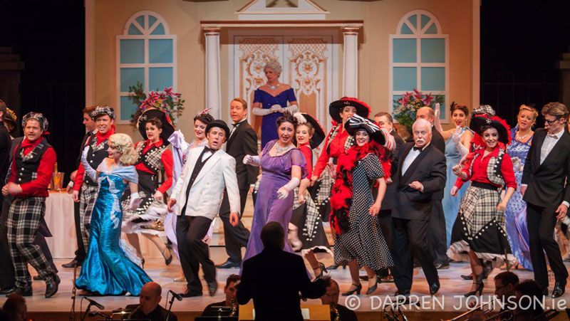 A large group of people are dancing on a stage in front of a conductor.