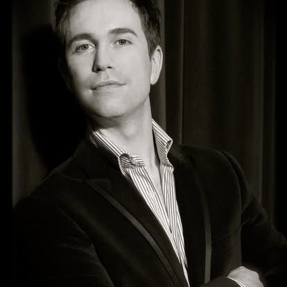 A man in a suit and striped shirt is standing in front of a curtain.