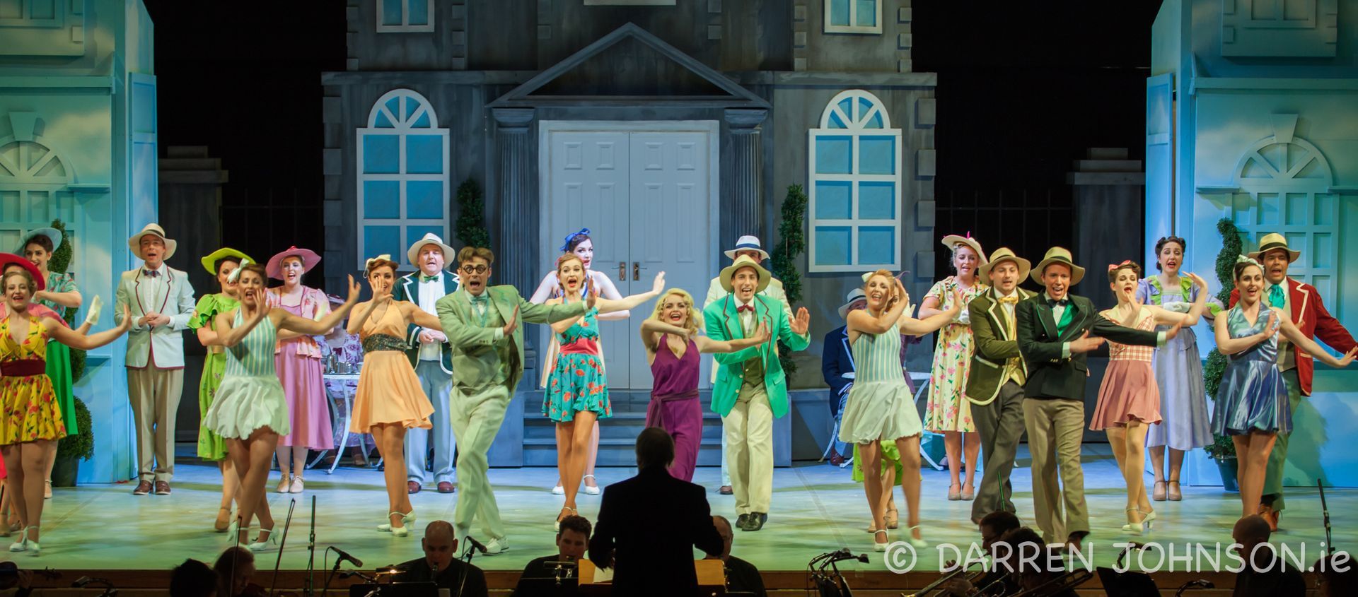 A group of people are dancing on a stage in front of a house.