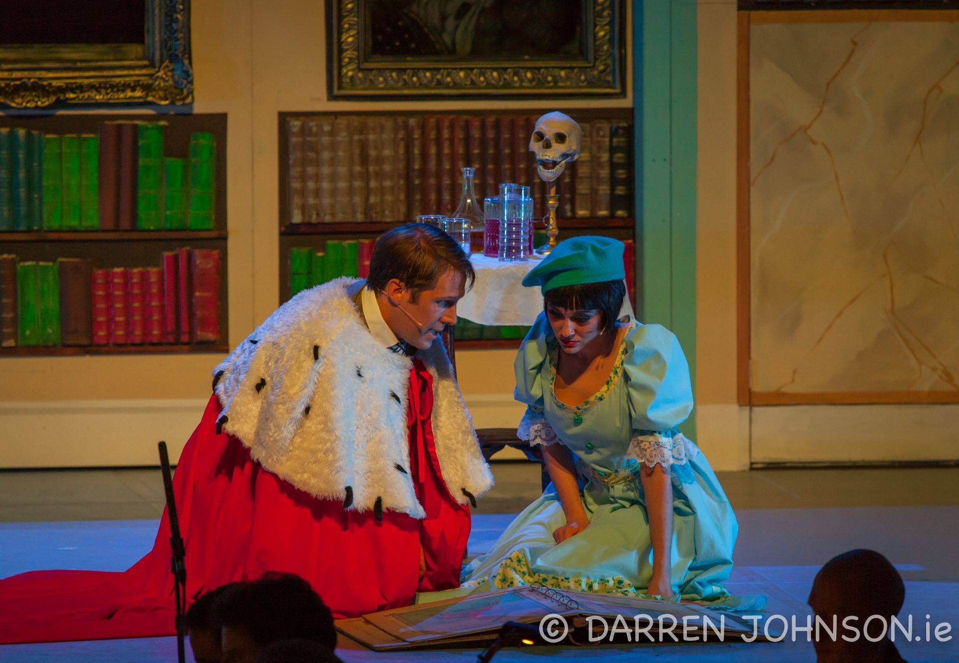 A man in a king 's robe is kneeling next to a woman in a blue dress.