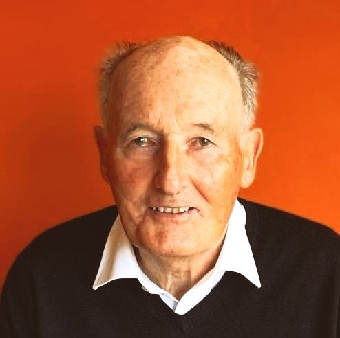 A bald man wearing a black sweater and white shirt smiles for the camera