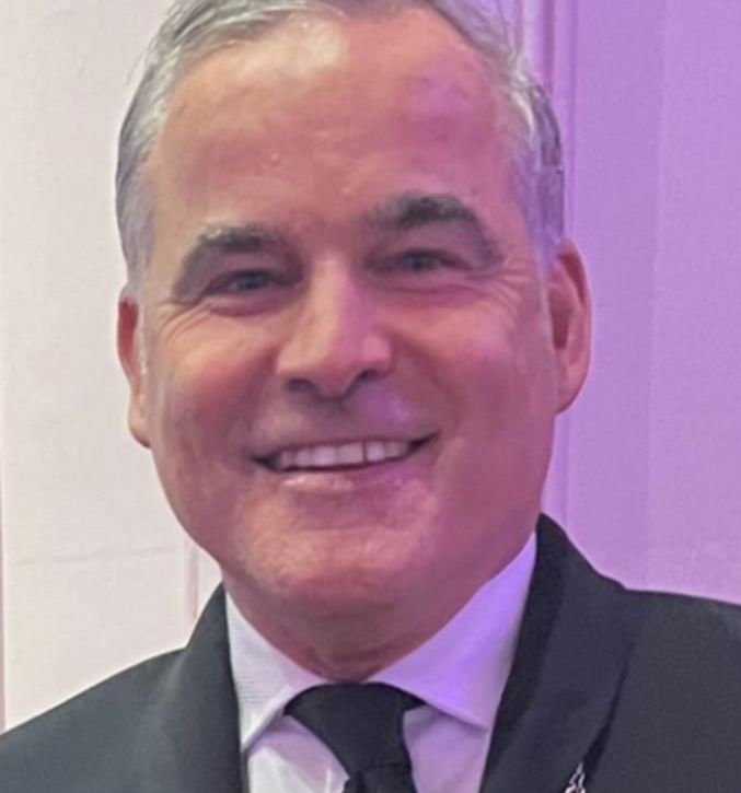 A man with gray hair and a blue shirt is smiling for the camera.