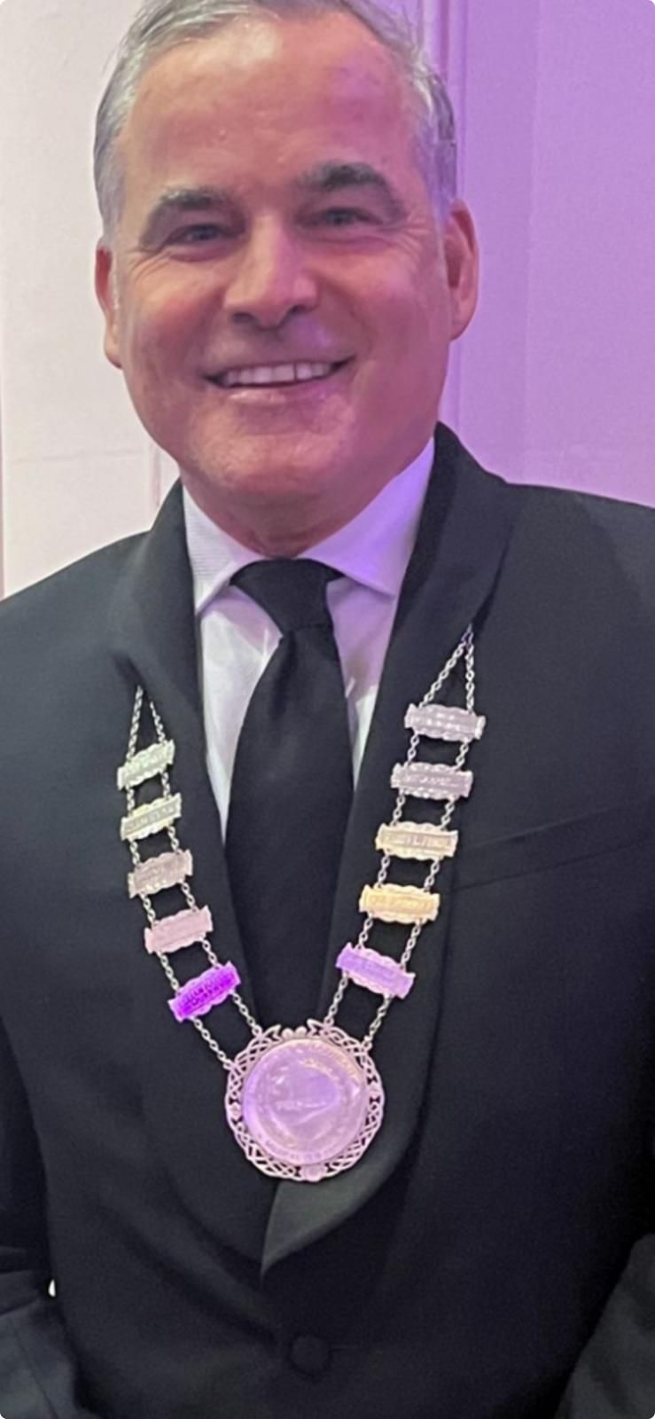 A man in a suit and glasses is standing with his arms crossed