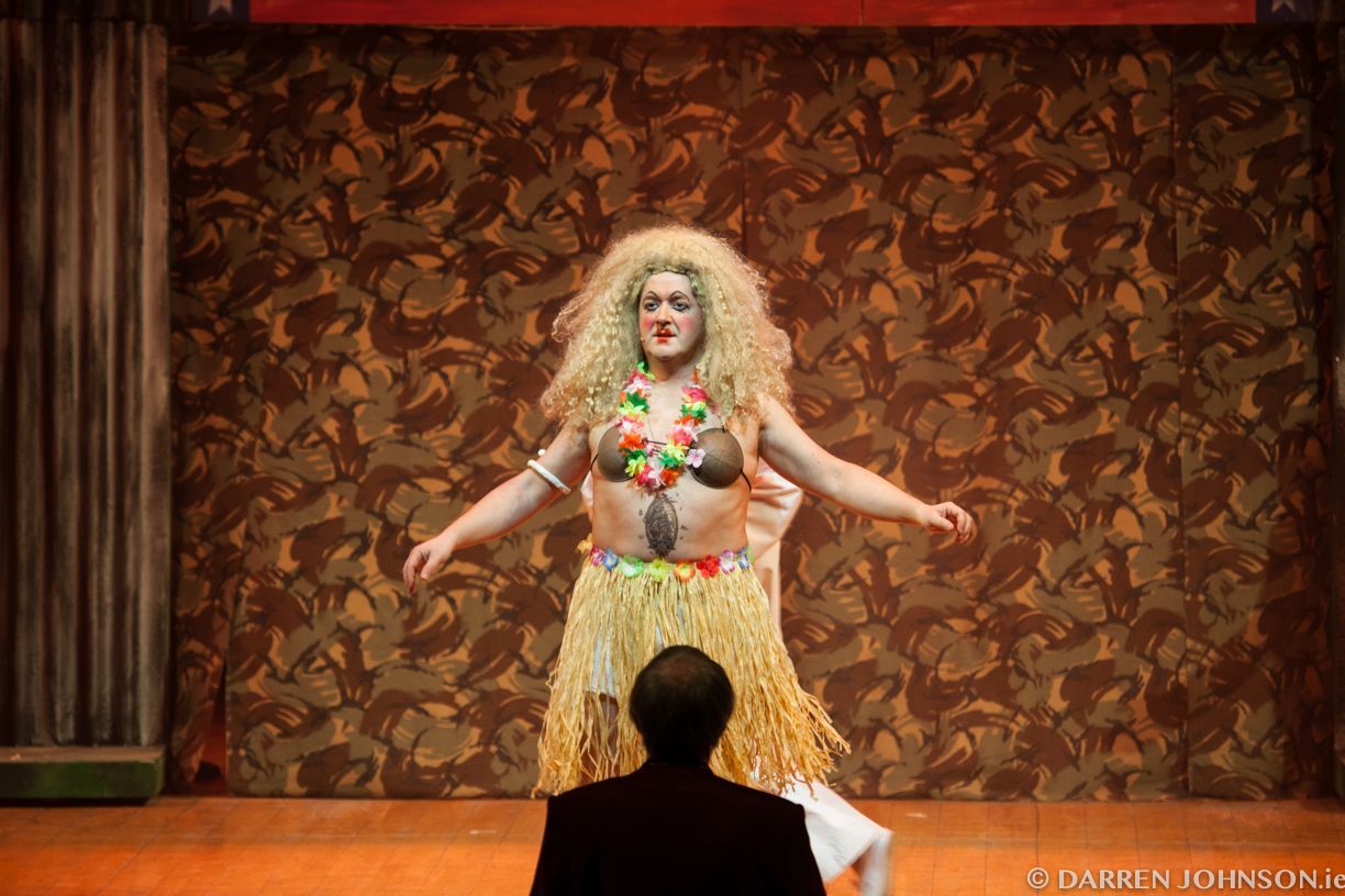 A man is watching a woman in a hula skirt on a stage.