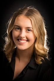 A man wearing glasses is smiling in front of a christmas tree.