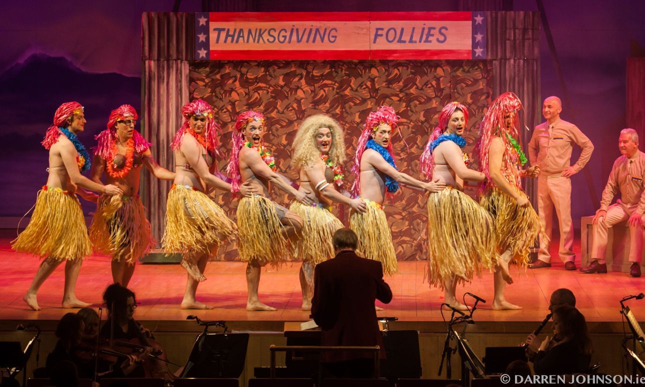 A group of men are dancing on a stage in front of a sign that says thanksgiving follies.