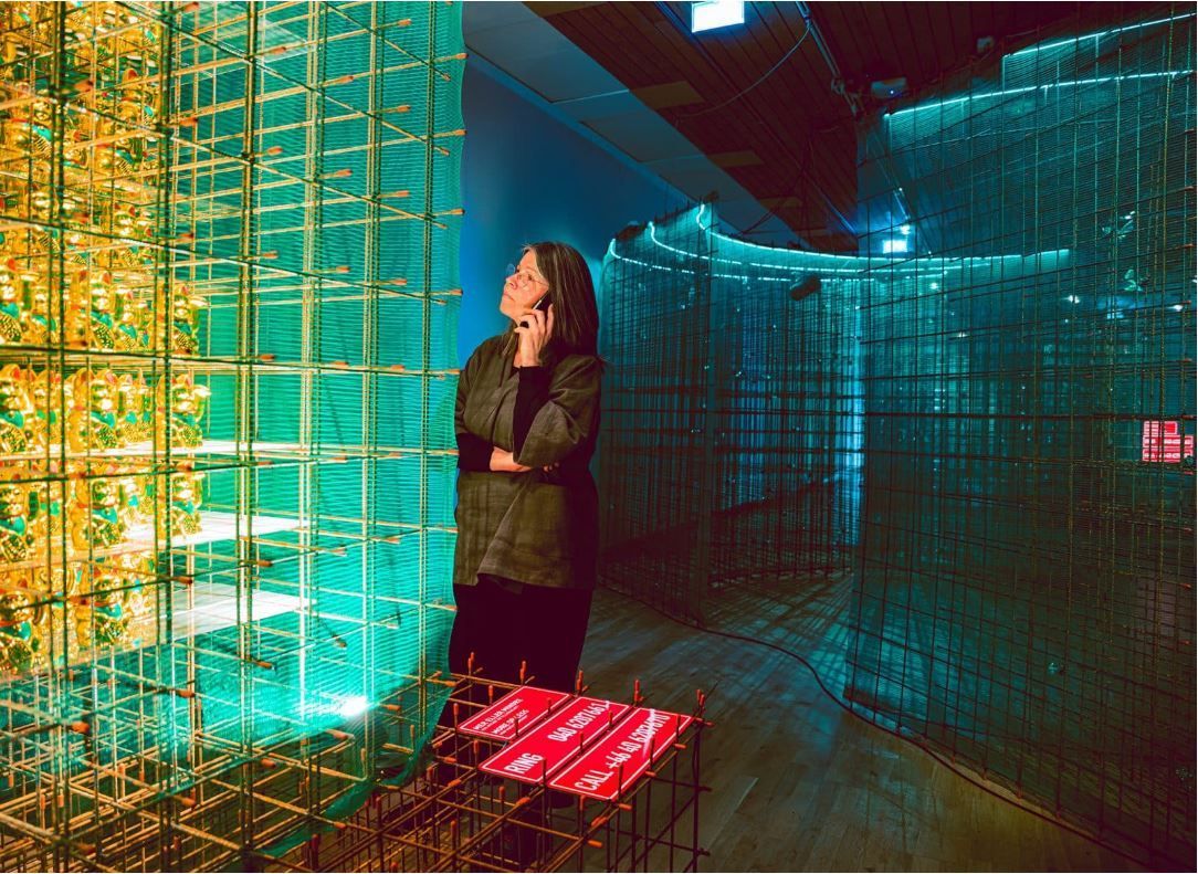 Visitor listing to the interviews on her phone while looking at the beckoning cat installation