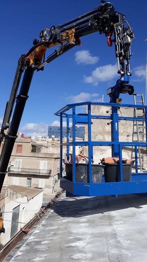 Una gru blu solleva una gabbia metallica