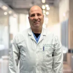 A man in a white lab coat is standing in a hospital hallway.
