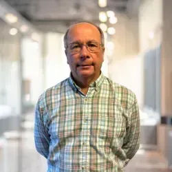 A man in a plaid shirt and glasses is standing in a hallway.