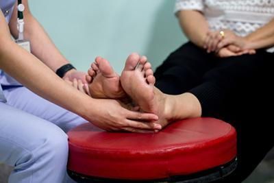 A woman is getting a foot massage from a nurse while sitting on a red stool.