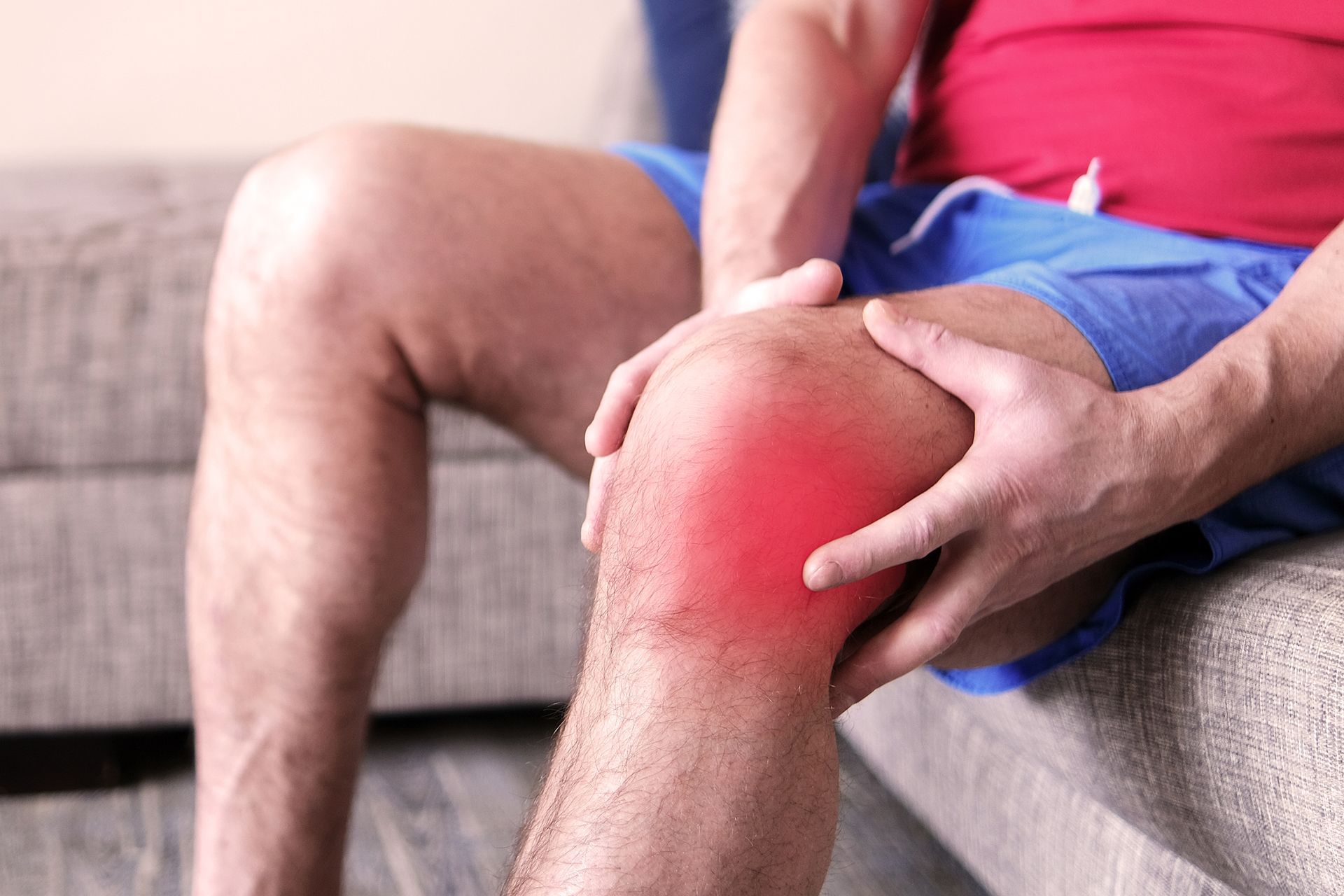 A man is sitting on a couch holding his knee in pain.