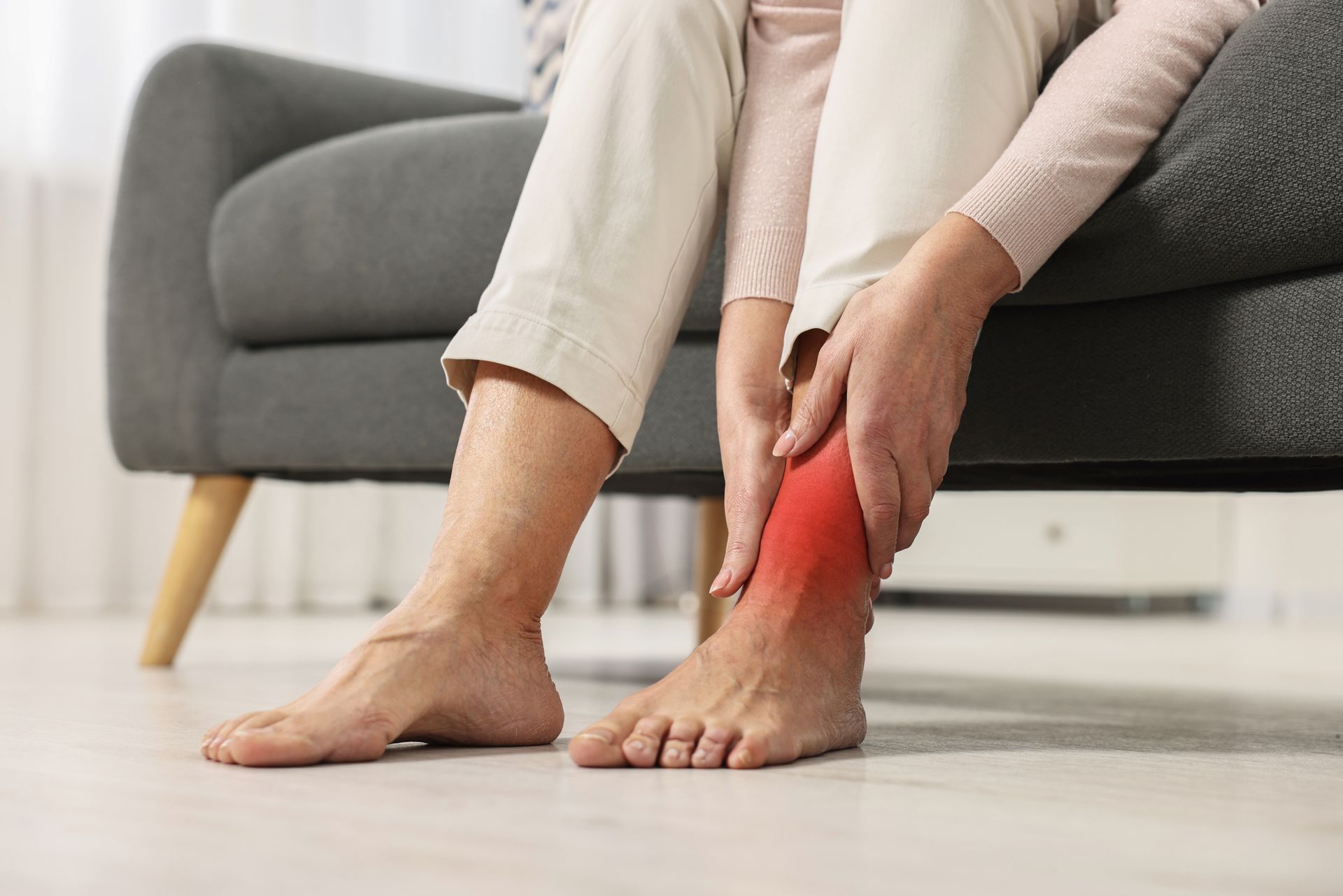A woman is sitting on a couch holding her ankle in pain.